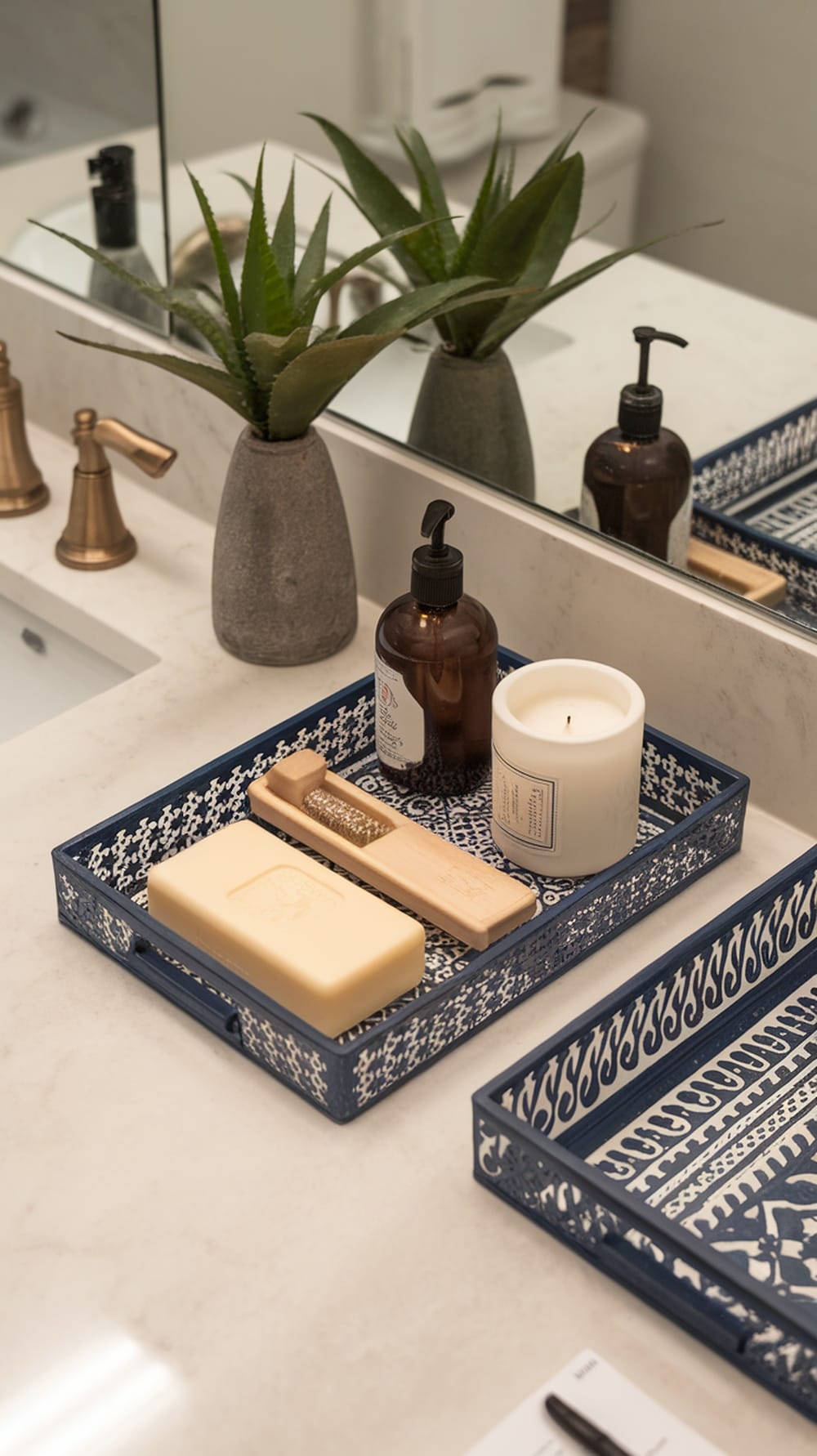 A decorative blue tray holding soap, lotion, a candle, and a wooden tool on a marble countertop with a plant in the background.